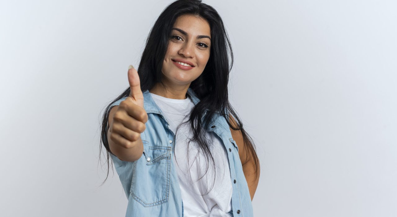 smiling young caucasian girl thumbs up looking at camera isolated on white background with copy space